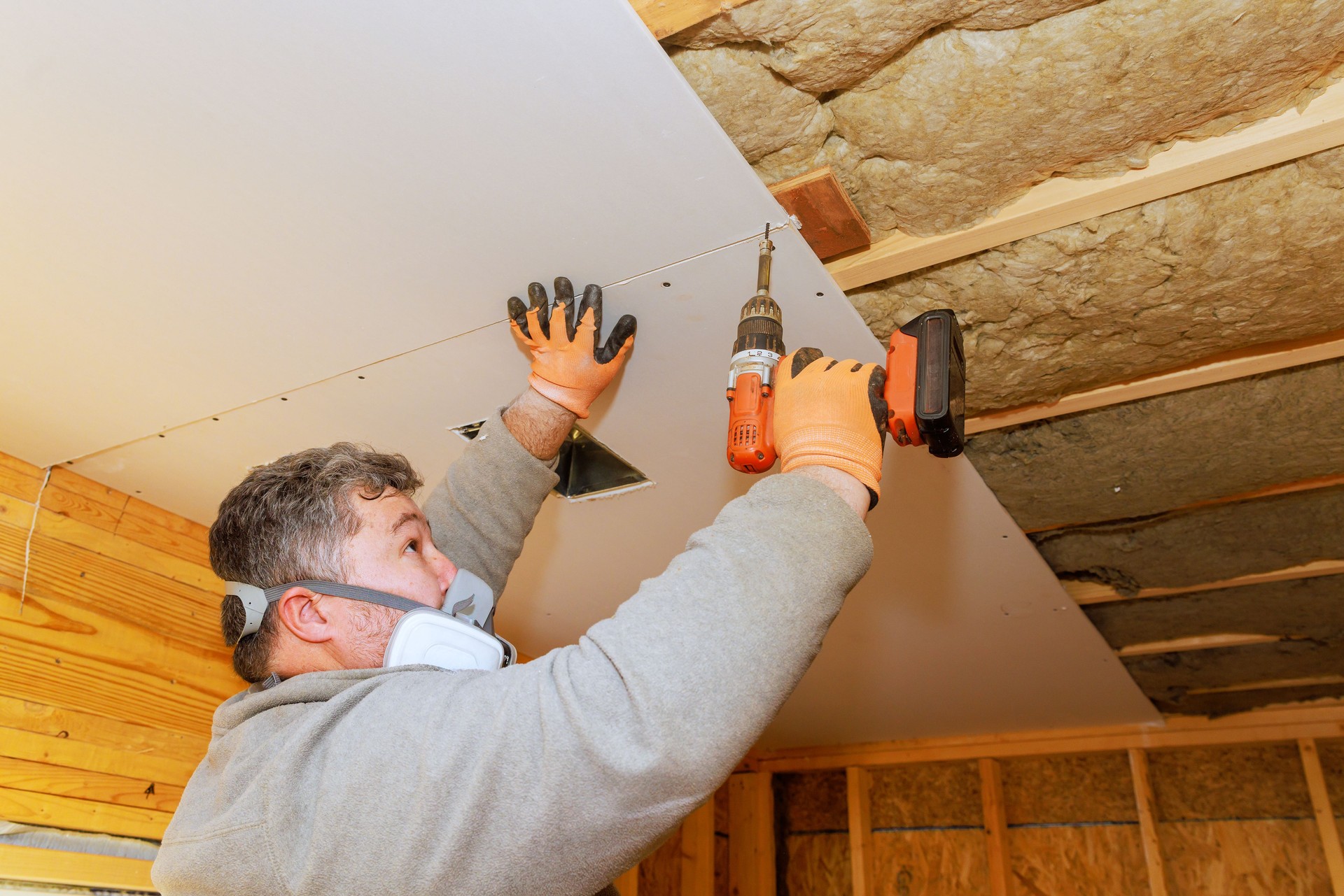 Construction worker installs drywall in interior space using power tools on a warm day